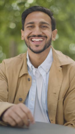 Vertical-Video-Portrait-Of-Smiling-Muslim-Man-Sitting-At-Outdoor-Table-On-City-Street